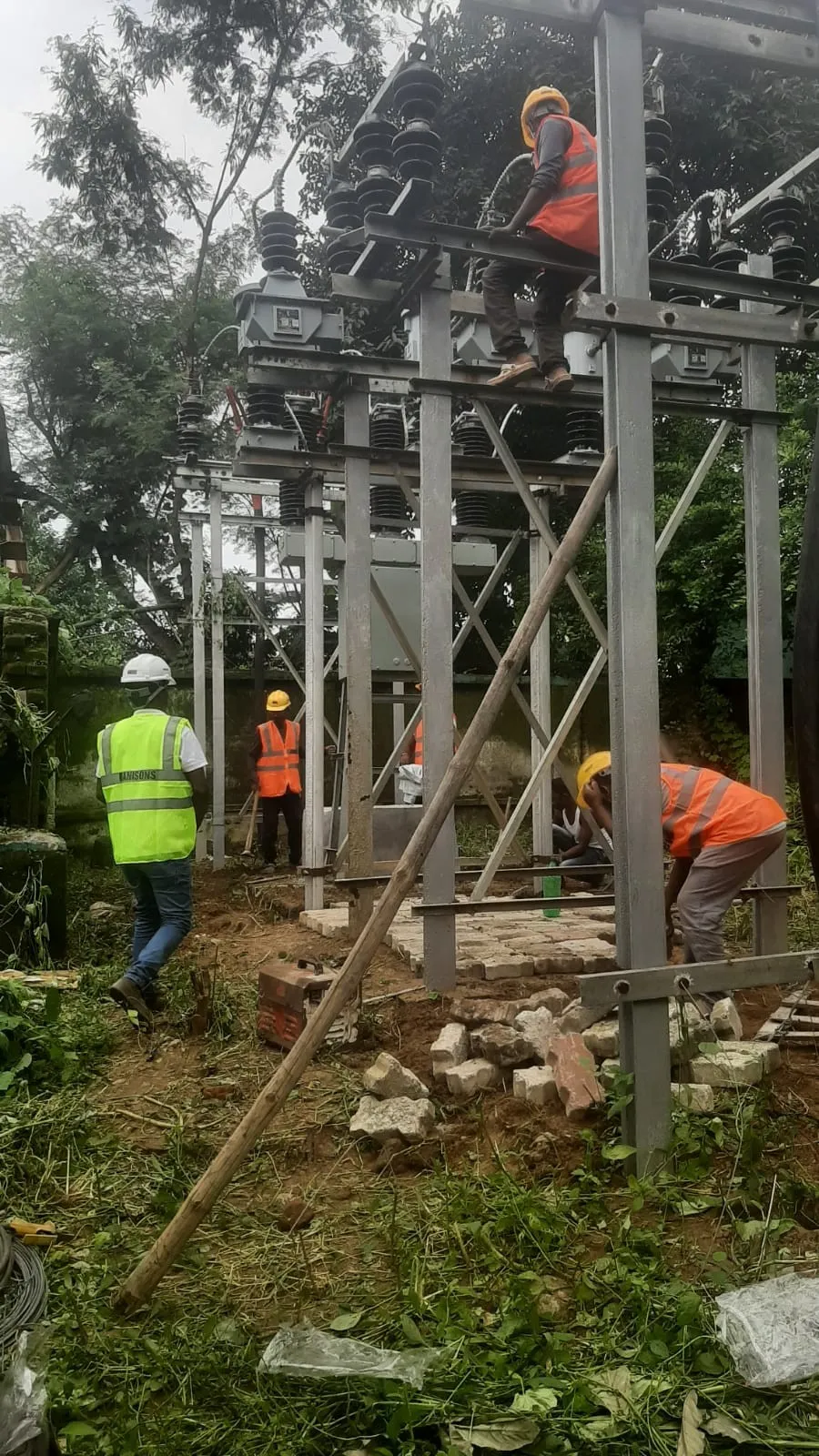 Steel gantry with cross-bracing under erection, workers at the base
