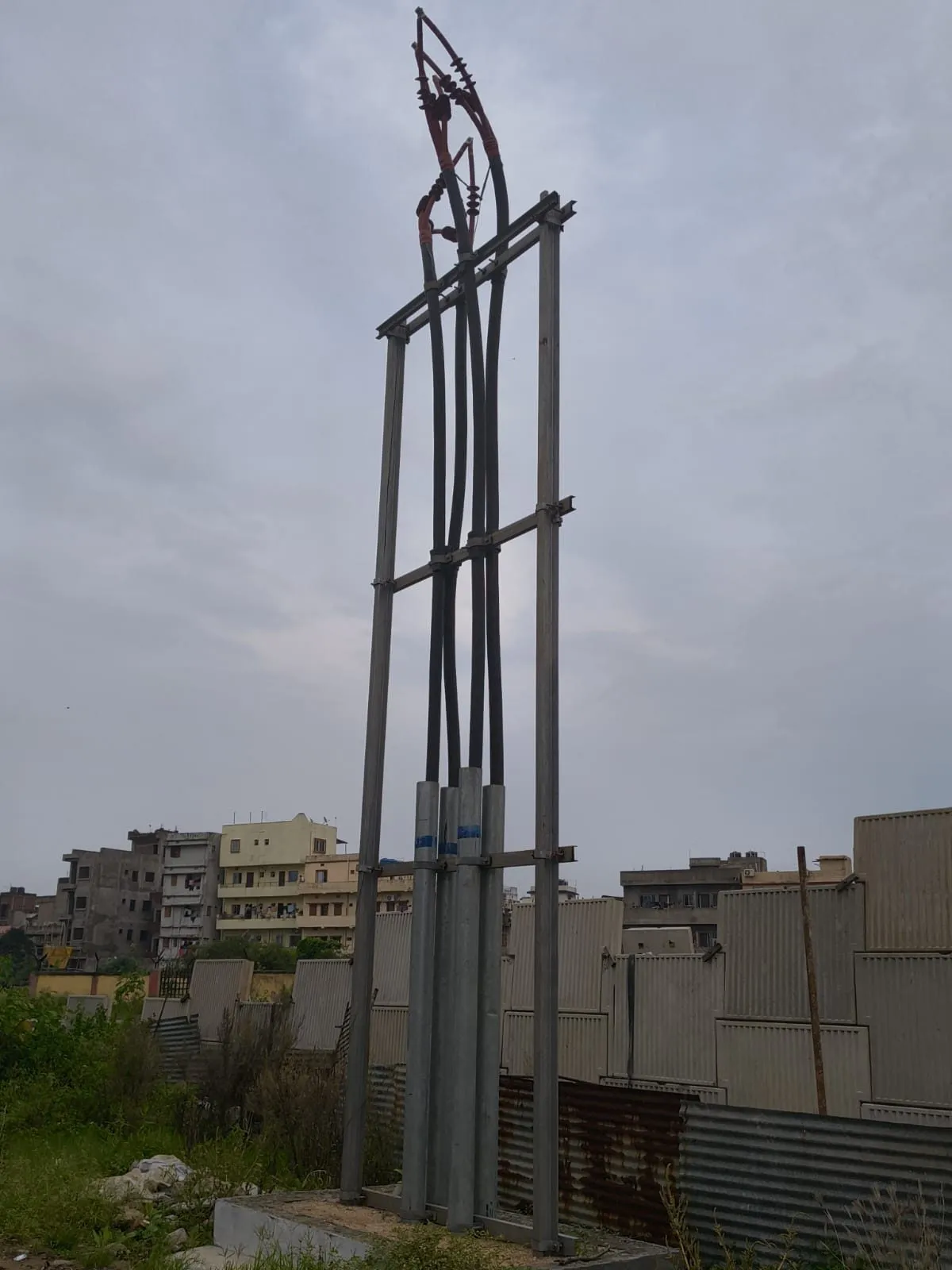 Steel HT gantry structure standing against an overcast sky above a boundary wall